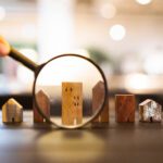 Hand holding magnifying glass and looking at house model, house selection, real estate concept.