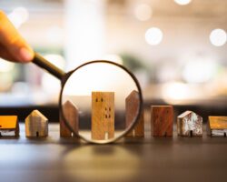 Hand holding magnifying glass and looking at house model, house selection, real estate concept.