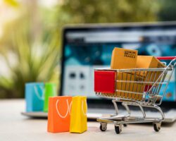 Product package boxes in cart with shopping bag and laptop computer with blurred web store shop on screen for online shopping and delivery concept