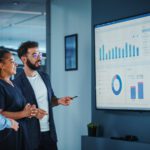 Company Operations Manager Holds Meeting Presentation. Diverse Team Uses TV Screen with Growth Analysis; Charts; Statistics and Data. People Work in Business Office.