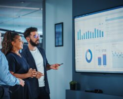Company Operations Manager Holds Meeting Presentation. Diverse Team Uses TV Screen with Growth Analysis; Charts; Statistics and Data. People Work in Business Office.